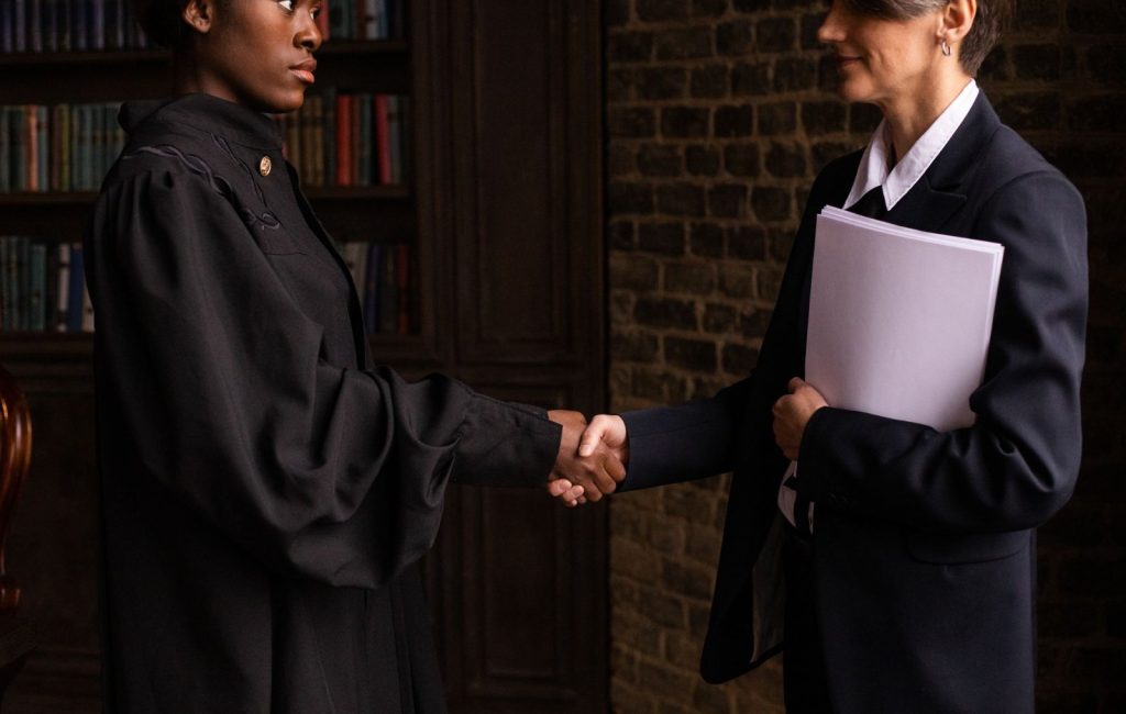Two people in business attire shaking hands, one holding a folder