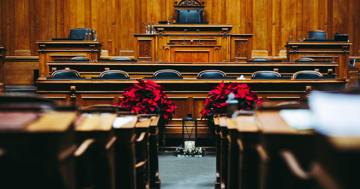 An empty wood-paneled courtroom with a judge's bench, seats, and red poinsettias.