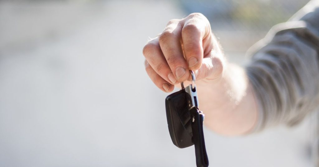 A hand holding out a set of car keys