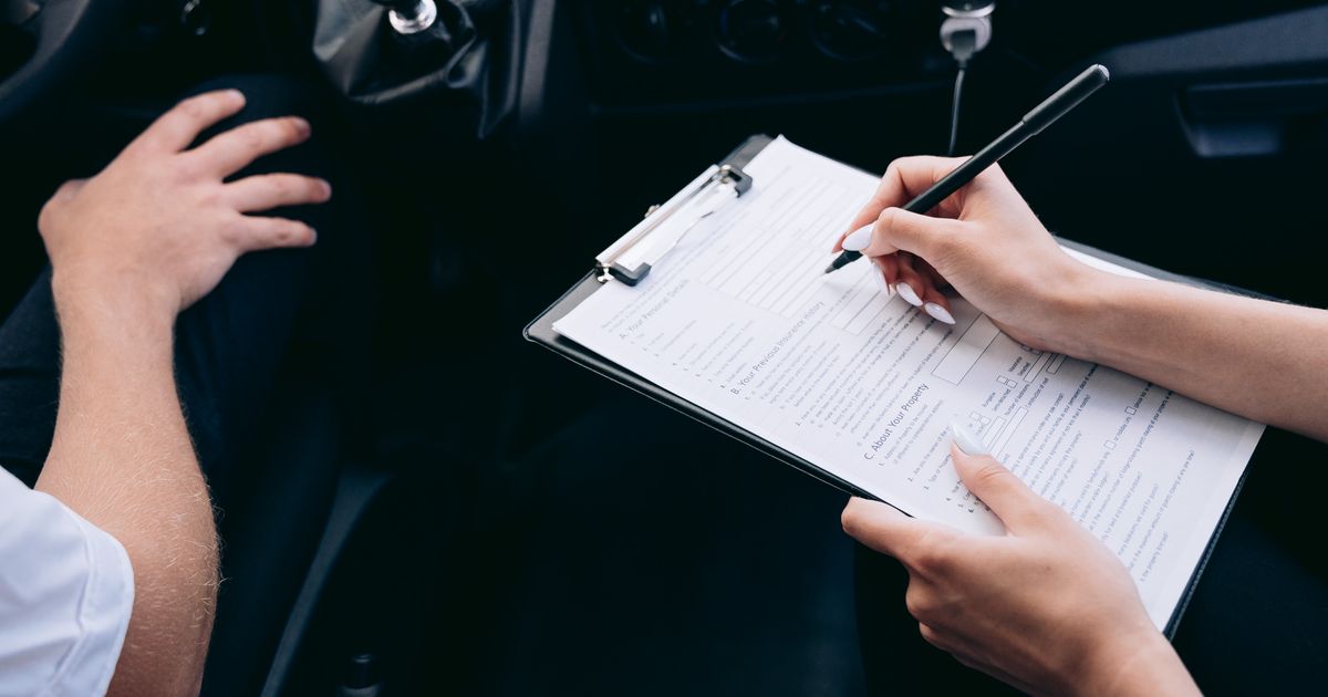 A person filling out a form on a clipboard inside a car