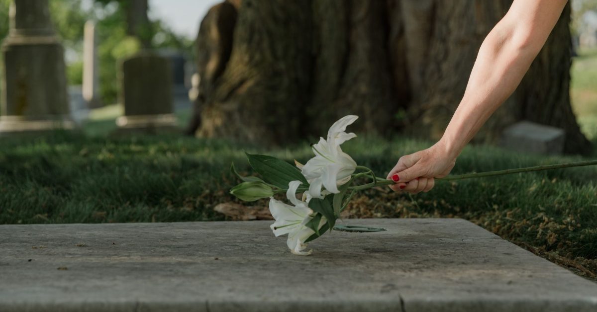 Person placing white lilies on a grave
