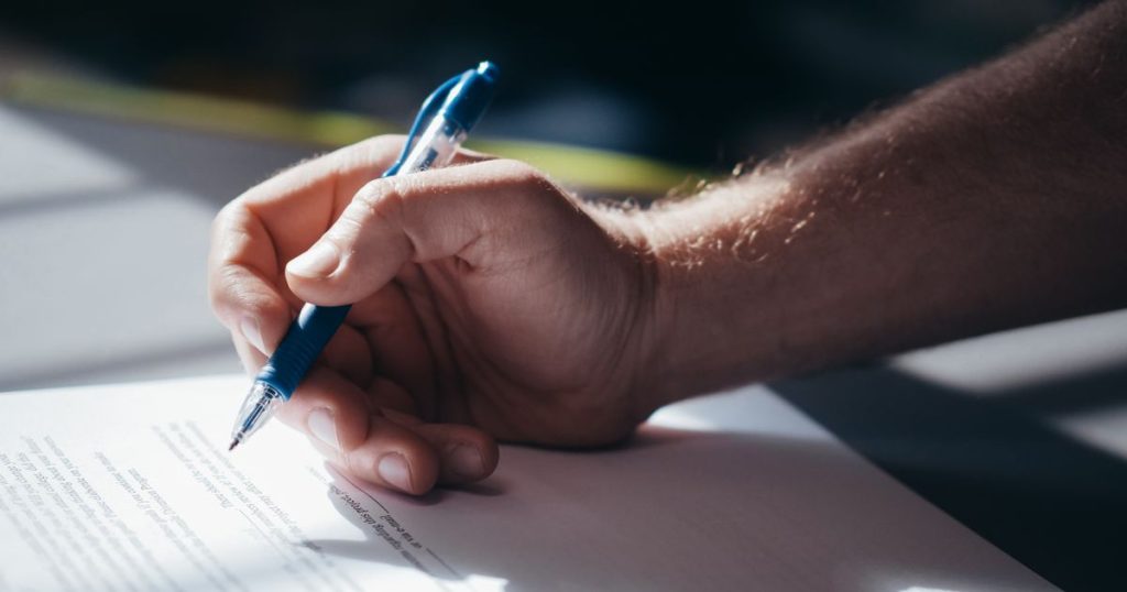 A person signing a printed document with a blue pen